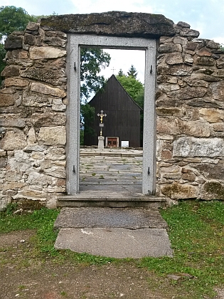Pohled přes někdejší kostelní dveře na opravenou hřbitovní kapli Svatého kříže v Hůrce a její interiér