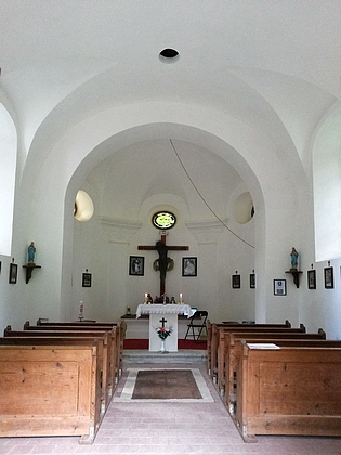 Pohled přes někdejší kostelní dveře na opravenou hřbitovní kapli Svatého kříže v Hůrce a její interiér