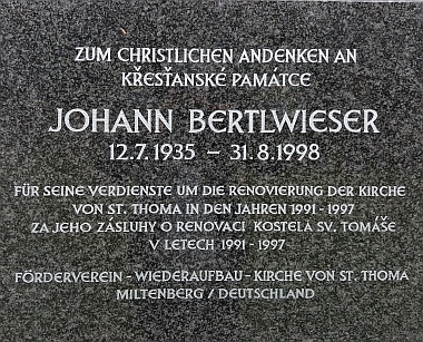Detail náhrobního kříže v místě jeho posledního spočinutí při hřbitovní zdi kostela ve Svatém Tomáši a pamětní deska k uctění Bertlwieserových zásluh o renovaci kostela ve Svatém Tomáši na jeho venkovní zdi