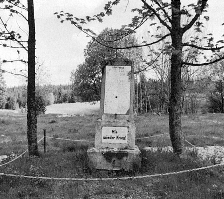 Památník padlým v Pohoří na Šumavě s nápisem "Už nikdy válku!", poškozený nahoře českým výstřelem a s horní částí zničenou - v místech za ním stávala zdejší škola