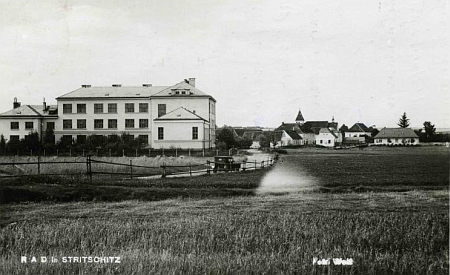 Strýčice s českou "jubilejní" školou, kde byla za války ubytována v rámci tzv. Říšské pracovní služby (RAD), na staré pohlednici fotoateliéru Wolf (viz i Matthäus Kraupatz)