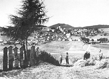 Městečko Lam při hoře Ostrý s Vysokým Bogenem v pozadí asi kolem roku 1930 prozrazuje neklamně "šumavský" ráz kraje, kde se odehrává román Rok se valí přes hory