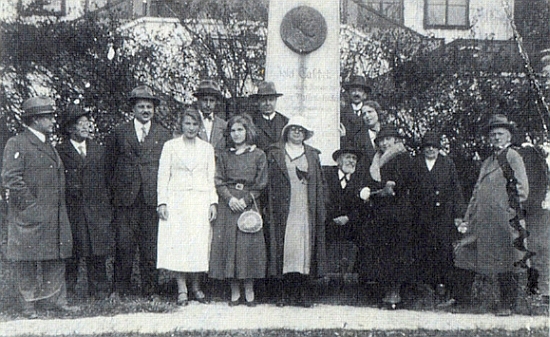 Zde je Taschek roku 1933 zachycen sedící při hořickém památníku, zobrazujícím na bronzovém reliéfu jeho vlastní podobu, jedna z mladých dívek stojících v popředí je pak Anna Mugrauerová, poslední představitelka Marie v meziválečných insenacích pašijových her, jejichž budova se zvedá za skupinou na snímku